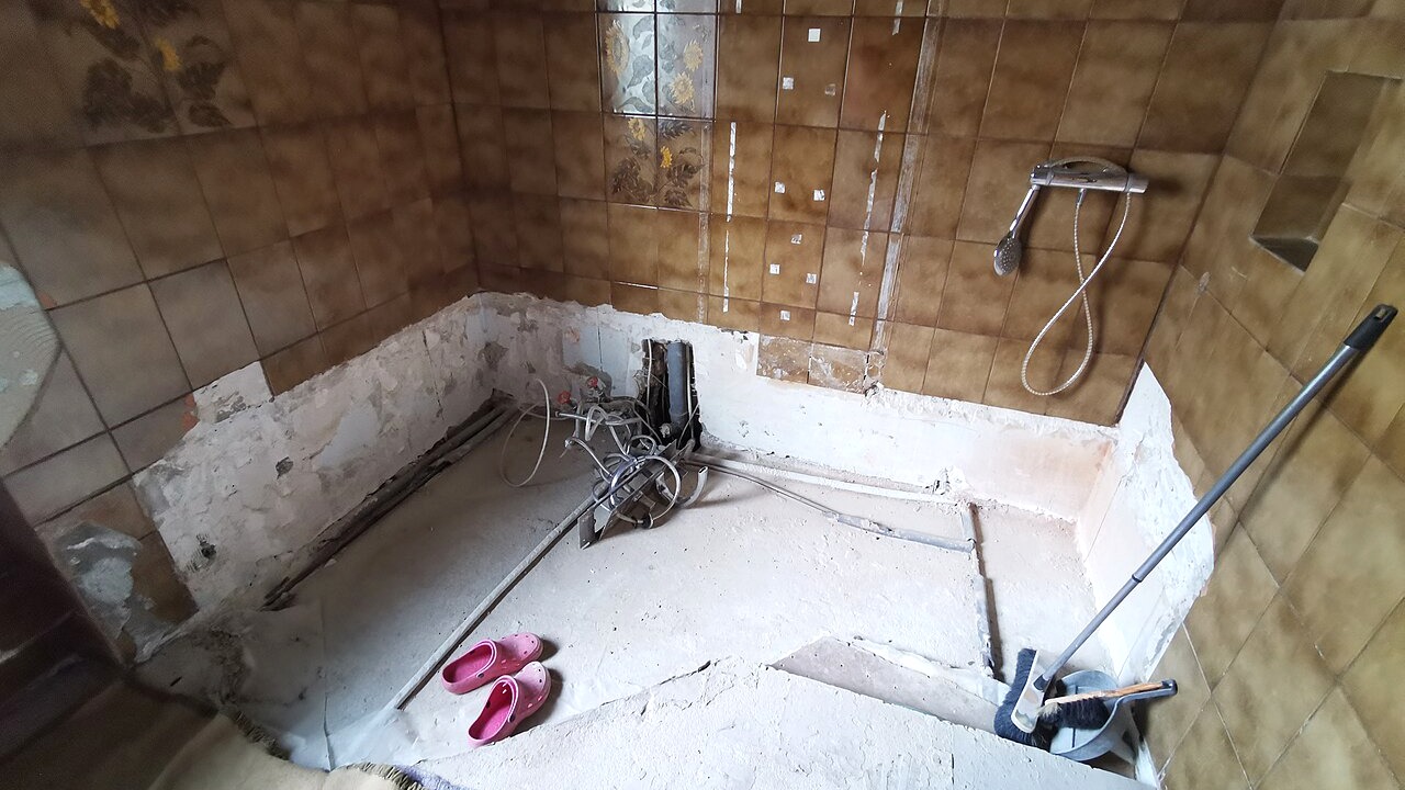 Salle de bain en phase de rénovation avec revêtements déposés et plomberie apparente